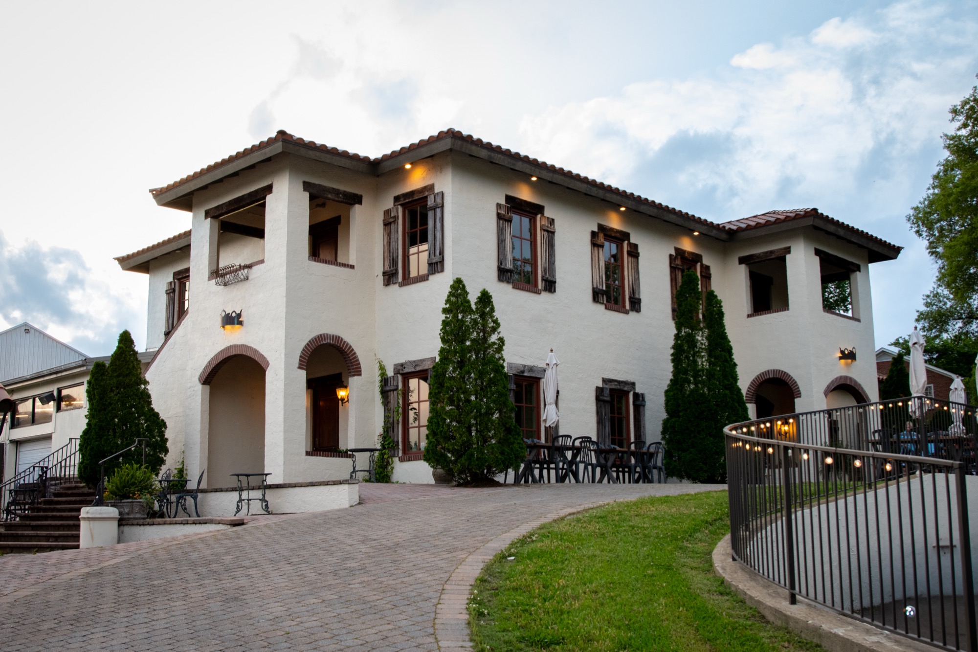 Large Tuscan inspired villa with white brick and red brown roof and a brick drive leading up