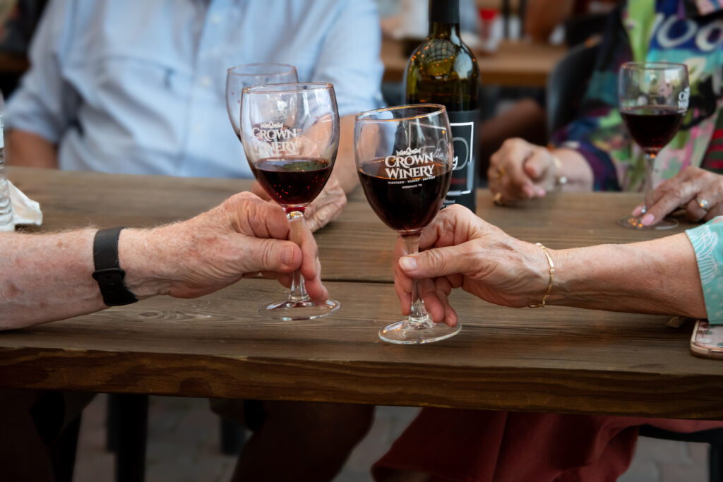 Older male and older female hands holding glasses of red wine from Crown Winery